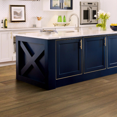 Modern kitchen interior featuring a navy blue island with gold accents, white countertops, and light wood flooring. The space includes white and navy cabinets, stainless steel appliances, and decorative elements like tulips and citrus fruits.